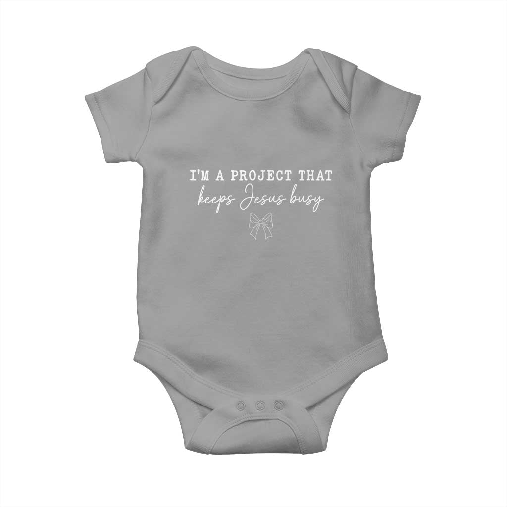 I am a Project That Keeps Jesus Busy Coquette Bow Baby Onesie Christian Faith Humor TS02 Sport Gray Print Your Wear